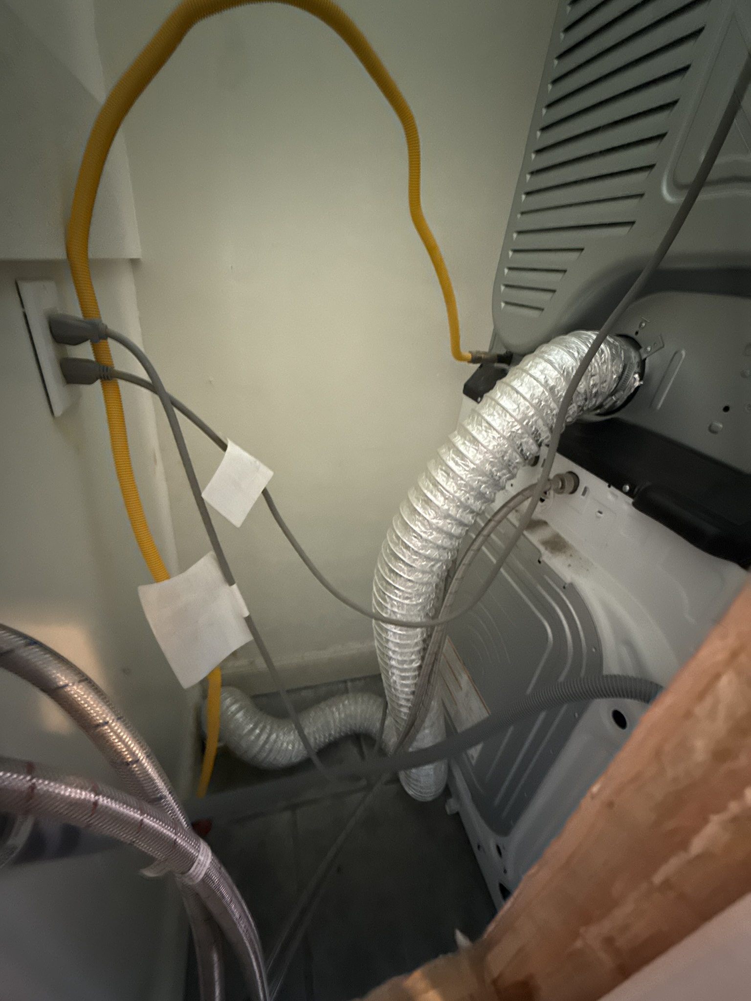 Interior laundry area showing a residential dryer positioned against a wall, with the exhaust connection area visible at the rear of the unit