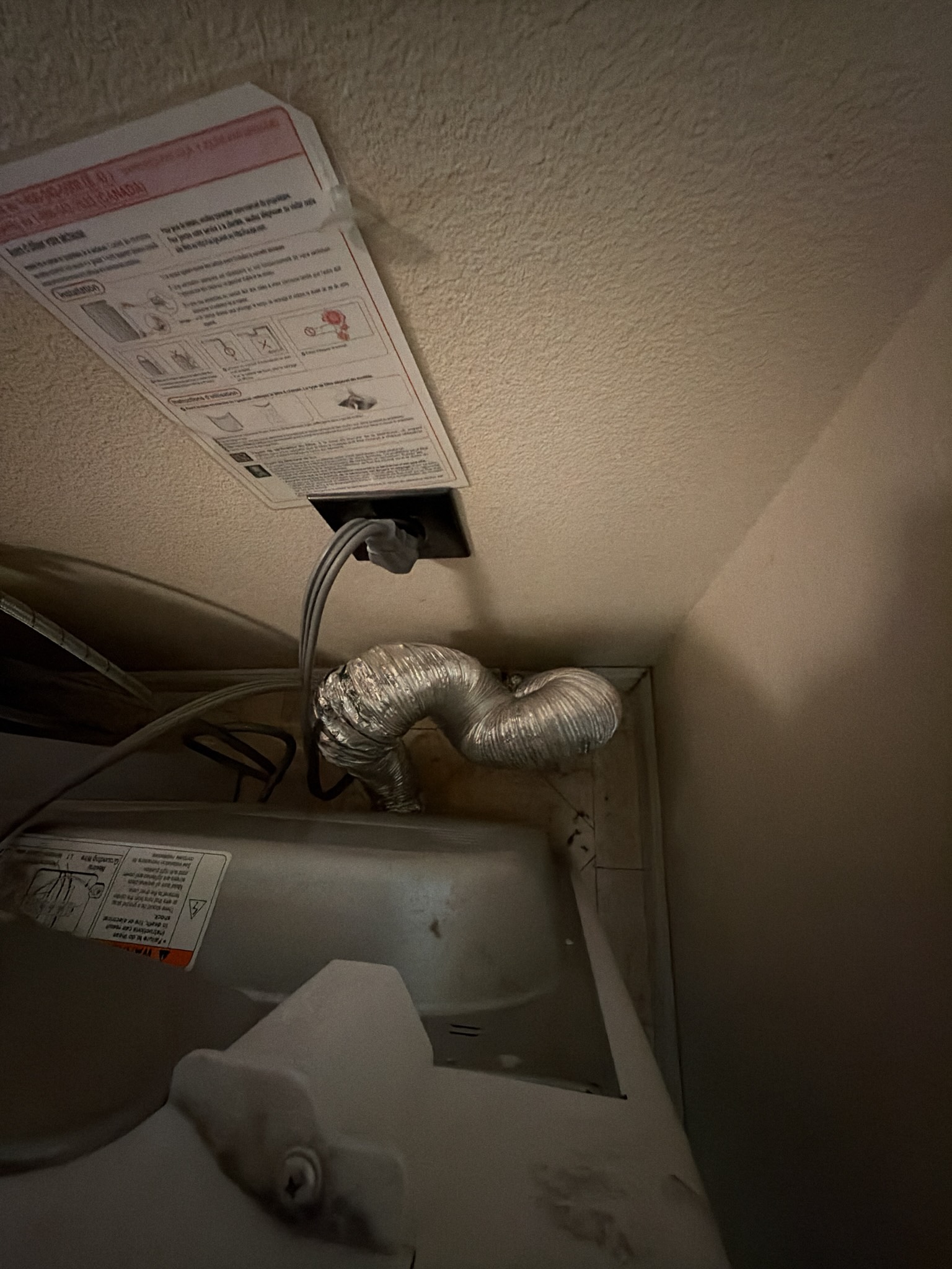 Dryer pulled away from the wall showing an old semi-rigid metal transition duct crushed and bent into tight folds with heavy lint buildup