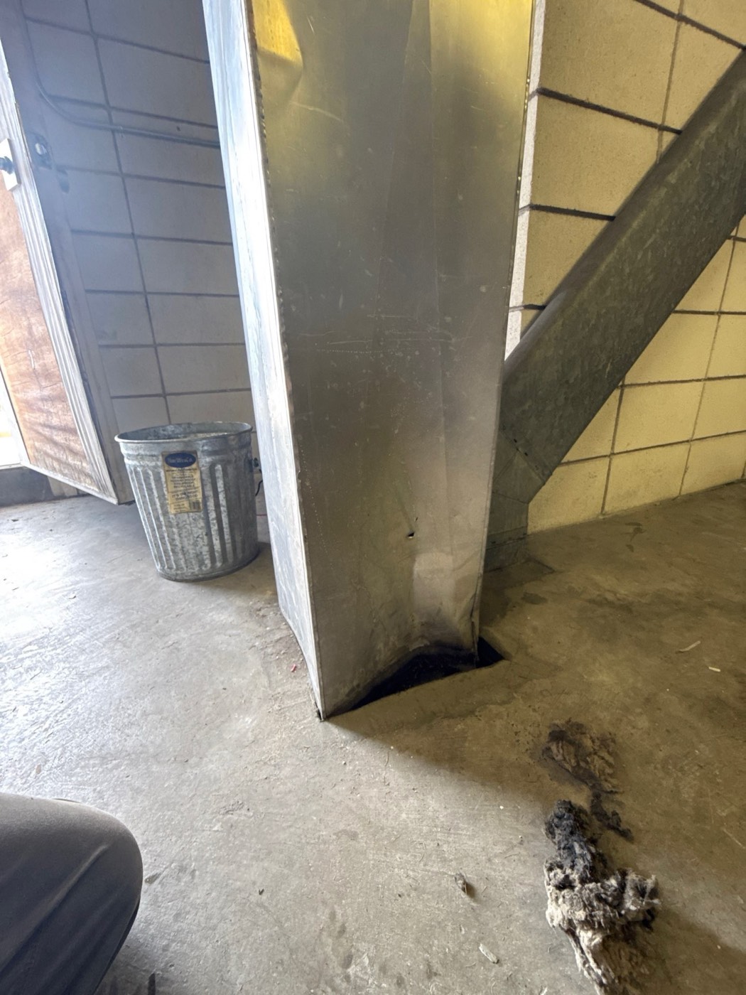 Large metal dryer vent duct shaft in apartment laundry room with lint debris on the concrete floor