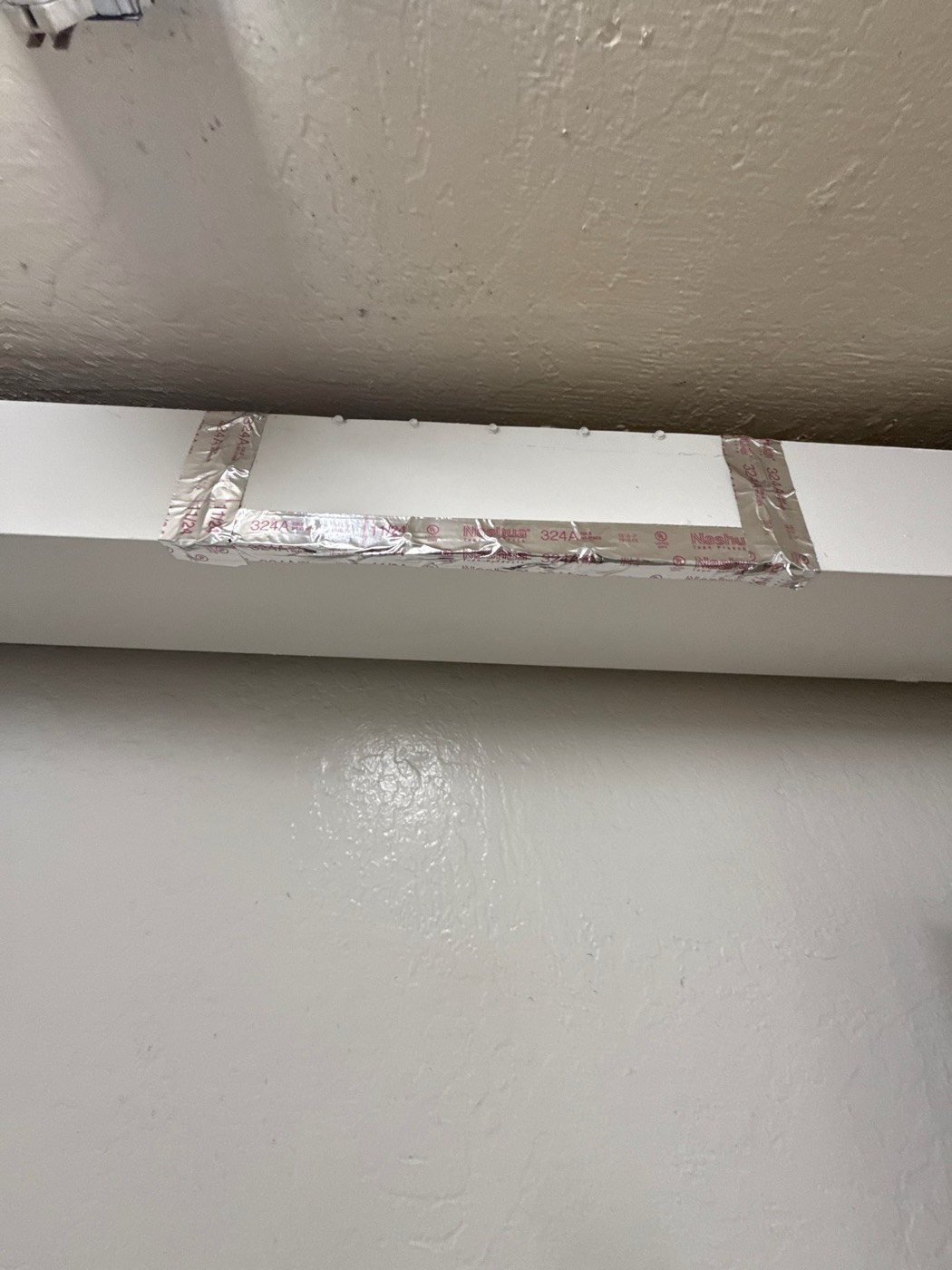 Dryer vent access panel sealed shut with Nashua foil tape above a doorway in an apartment building