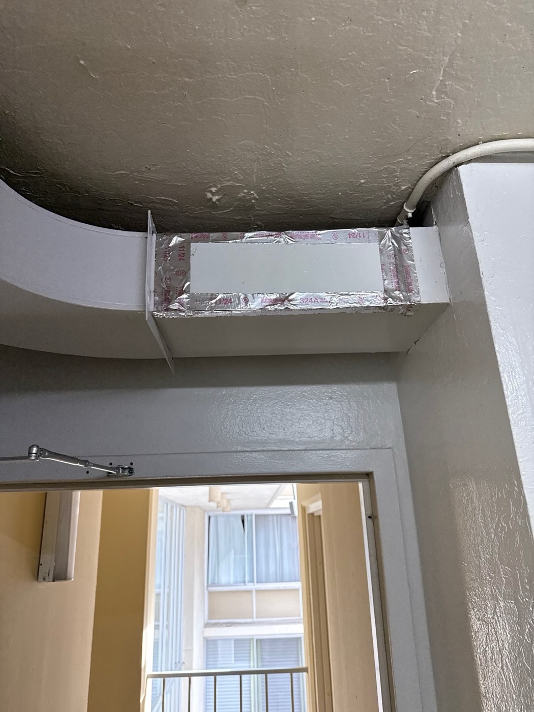 Dryer vent ductwork access panel taped shut with Nashua foil tape at a bend in the duct run
