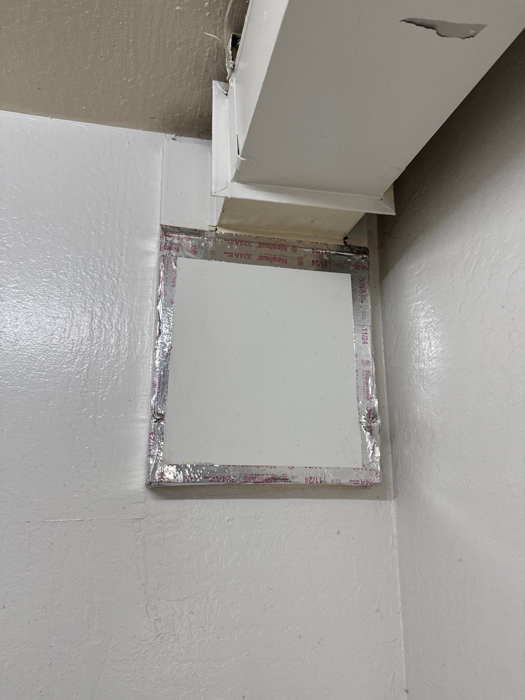 Square dryer vent access panel sealed with foil tape in the corner of the laundry room ceiling